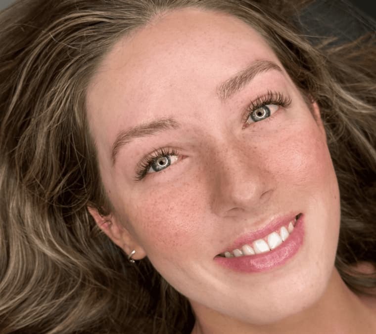 Smiling woman with fresh lashes, defined brows, and glowing skin after facial treatment